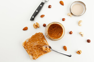 Bread with peanut butter. Jar of peanut butter. Jar lid, spoon, knife and different types of nuts. Cashew, almond, walnut, hazelnut, isolated on white background.