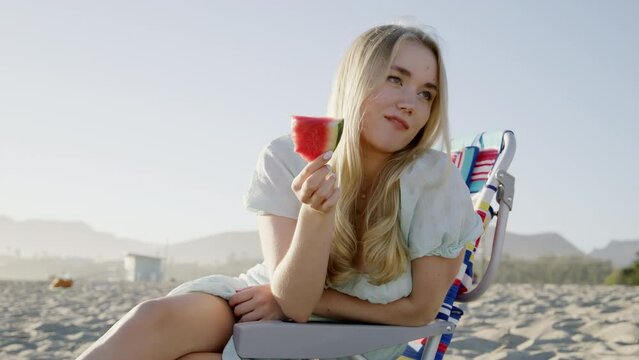 Beautiful girl enjoys fresh berry within stunning natural landscape. Cheerful, laughing woman eating flavorous snack with sandy beach in the background. High quality 4k footage