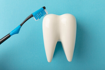Fototapeta na wymiar Cleaning model of a white tooth with a toothbrush on a blue background. The concept of dental hygiene. Prevention of plaque and gum disease.Prevention of caries.MOCKUP