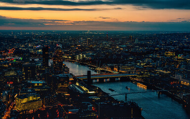 Aerial view of west London, blue hour just after sunset, orange yellow street lights starting to glow, river Thames separating two shores