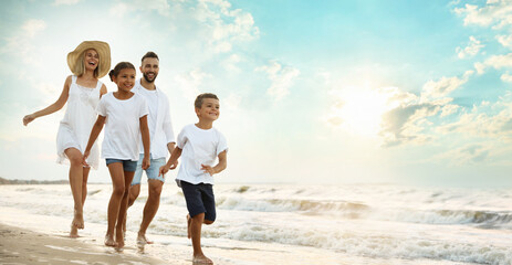 Happy family walking on sandy beach near sea at sunset, space for text. Banner design