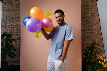 Happy young pediatrician holding balloons over pink background