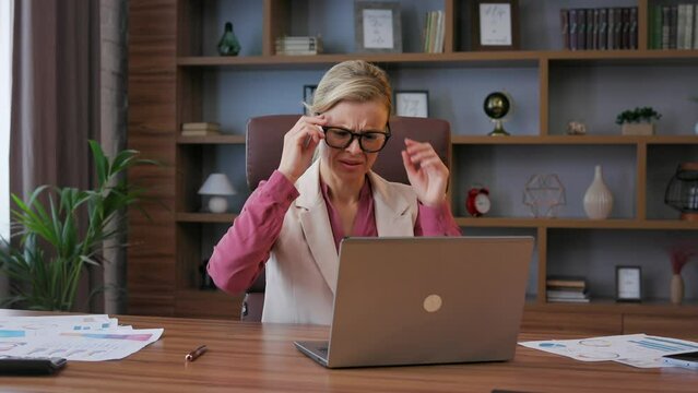 Depressed businesswoman overworked on laptop computer. Tired worker recieved bad online news, close the laptop, put off eyeglasses. Financial crisis, bankruptcy, burnout syndrome, depression, apathy.