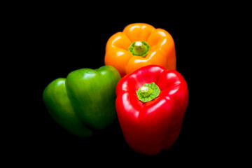 three different colored peppers: red, green and yellow peppers lie on a black background