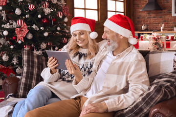 Happy 50s older couple using digital tablet in living room on Christmas. Smiling mature...