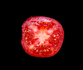 A sliced red tomato lies on a black background