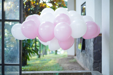 A beautiful bunch of pink and white balloons floating outdoors in a sunlit garden, a whimsical...
