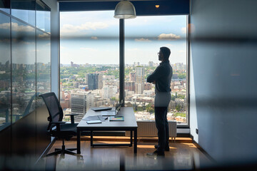 Silhouette of businessman standing in office with big city capital urban view.