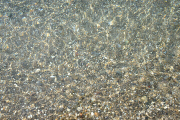 Shimmering sun glares on pebble seabed under water as background.