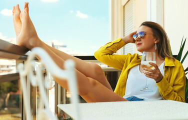 Woman with white wine enjoys her vacations on the balcony.