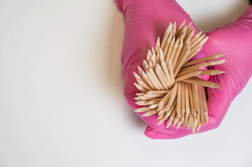 Master in pink gloves holds orange sticks for manicure. 