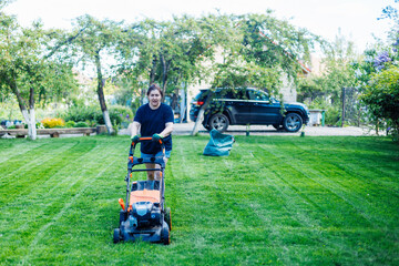 Dark-haired female gardener in casual clothes using lawn mower or grass cutter in the yard, grounds. Technological machine for lawns. Cutting fresh lush green grass in countryside. Grass equipment