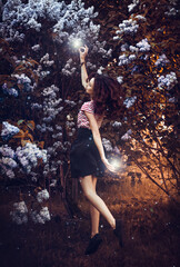 Fantasy girl in levitation with a soaring magic ball. In a fairytale forest on alley with flowers