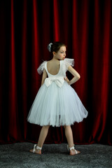 A cute ballerina girl in a white dress on a red background. Art. Dance. Beauty.