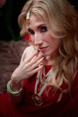 A beautiful European girl looking like an Arab woman in a red room in a harem. Photo shoot of an oriental style odalisque. A model poses in a sari as an indian woman in india