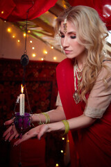 A beautiful European girl looking like an Arab woman in a red room in a harem. Photo shoot of an oriental-style odalisque. A model poses in a sari