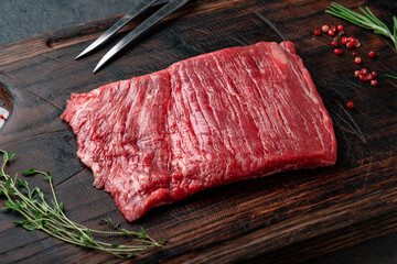 Raw flank steak on a wooden board with grilling seasonings, close up - obrazy, fototapety, plakaty