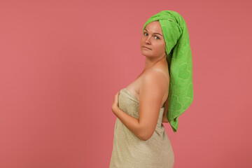 a young woman after a shower in a green towel on her head stands sideways on a colored background