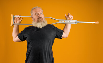 disabled man with a gray beard put a crutch on his shoulders on a yellow background