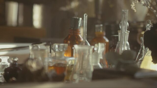 Close-up of a perfumer's workplace. Vintage cinematic concept. Sunny day in the working workshop. Lots of ingredients, a book, glass flasks on the table. Depth of field. 4K video