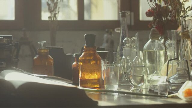 Close-up of a perfumer's workplace. Vintage cinematic concept. Sunny day in the working workshop. Lots of ingredients, a book, glass flasks on the table. Depth of field. 4K video