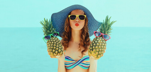 Portrait of young woman blowing her lips sending air kiss with two funny pineapples with sunglasses...