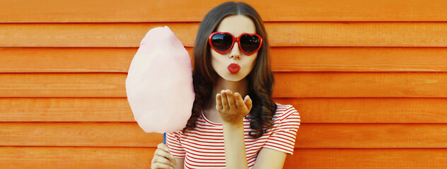 Portrait of sweet young woman blowing her lips sending air kiss with cotton candy wearing red heart...