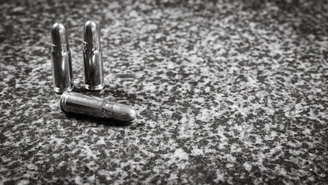 three Tokarev pistol (TT) cartridges (7.62×25mm) on a gray granite background, monochrome photo