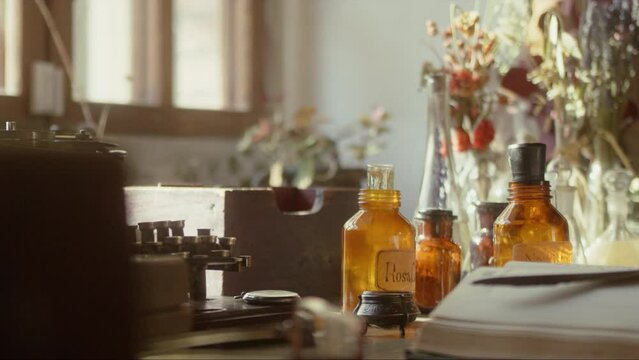 Close-up of a perfumer's workplace. Vintage cinematic concept. Sunny day in the working workshop. Lots of ingredients, a book, glass flasks on the table. Depth of field. 4K video