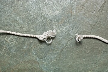'Tension concept with frayed ends  of snapped white braided rope  hanging against  rock face'
