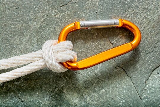 'Close up of white braided rope lashed to carabiner set against rock face'
