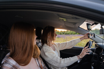 Two young women laughing in the car during a summer road trip. Best friends have fun together as they drive through the countryside. A happy couple of girls relaxing on a road trip.