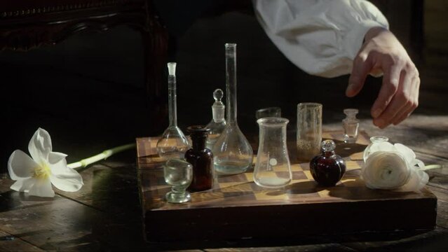 A man's hand plays chess with flasks on a chessboard. The concept of a perfumer, relaxation, creative crisis, reflection, play, invention. Cinematic concept. Close-up. 4K video, RED camera