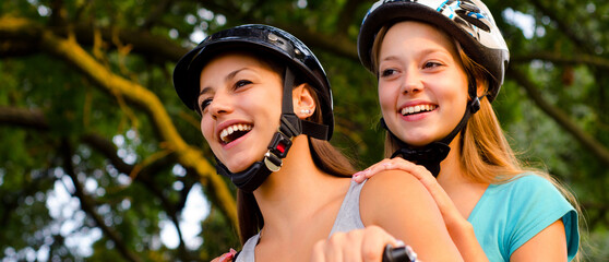 Two smiling happy teenage girls riding scooter motorcycle on sunny summer day
