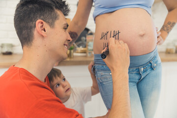 Obraz na płótnie Canvas man writing lines on his wife belly and counting pregnancy weeks, family concept. High quality photo