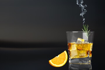 Whiskey or cognac in cristal glass with smoked rosemary, and slice of orange. Alcoholic drink.