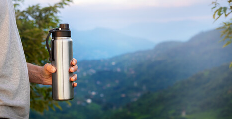 Man traveller holds silver thermos mug and looking into mountains on background, concept of outdoor...