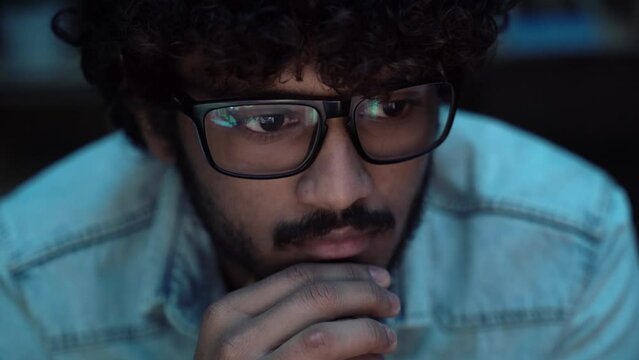 Indian crypto trader analyst wearing eyeglasses working looking at computer screen reflecting in glasses analyzing online trading stock exchange market data charts. 