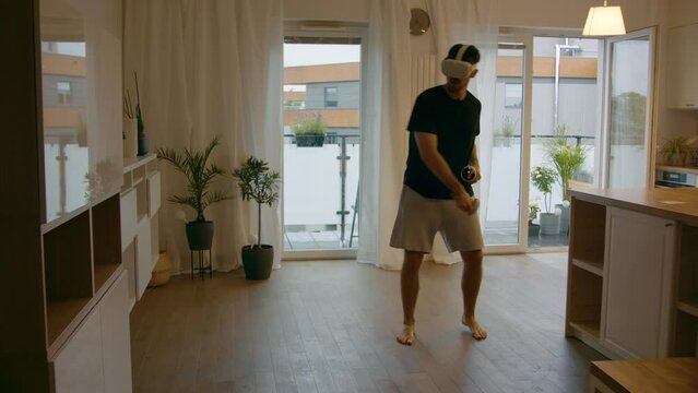 Fit mid 30s Caucasian male using metaverse VR 360 headset, playing tennis workout game at home