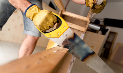 carpenter working on a construction site sawing a strip of wood with his hand saw.
