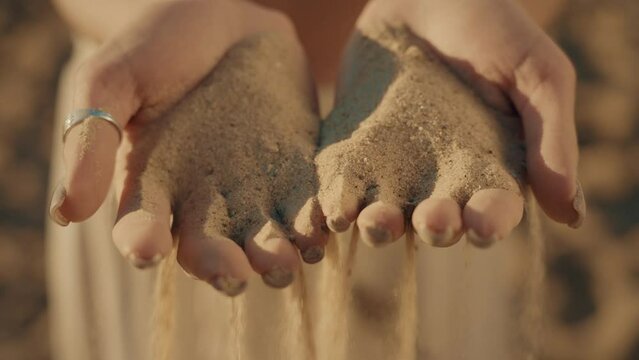 4K Cinematic brown video of woman hands with sand. Sunset or surise light. Dessert and holiday consept.