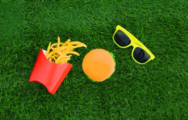 Fast food concept - burger, french fries and sunglasses on the grass background
