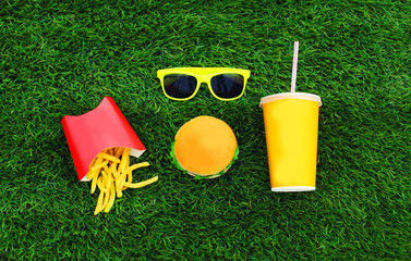 Fast food concept - burger, french fries and cup of juice on the grass background