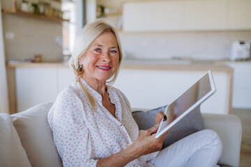 Senior woman sitting on sofa and rusing tablet at home