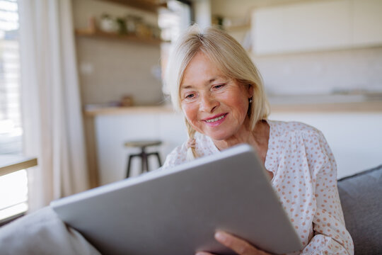 Senior woman sitting on sofa and rusing tablet at home