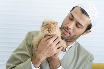 Handsome muslim man holding lovely brown cut furry kitten in own hand looking attention their...
