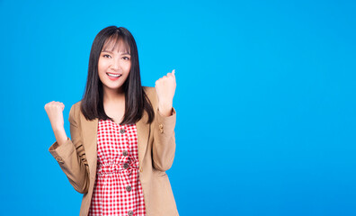 Excited business asian woman holding fist arms hand smile happiness success job or lucky standing over isolated blue background. Positive girl raised arms hand for new job. Lifestyle, winner concept.