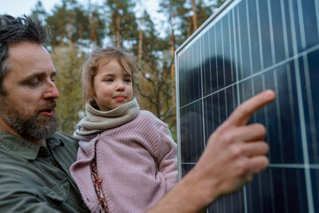 Portrait of father and daughter holding a solar panel in garden.