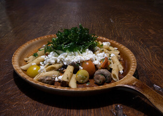 Fried noodles with mushrooms, tomato and feta cheese on a brown plate for menu in the restaurant or cafe copy space