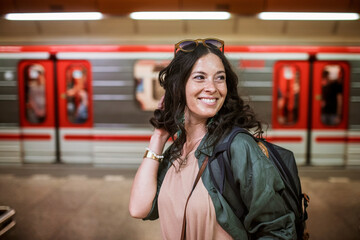 Mid adult woman commuter is standing in subway station and looking at camera.